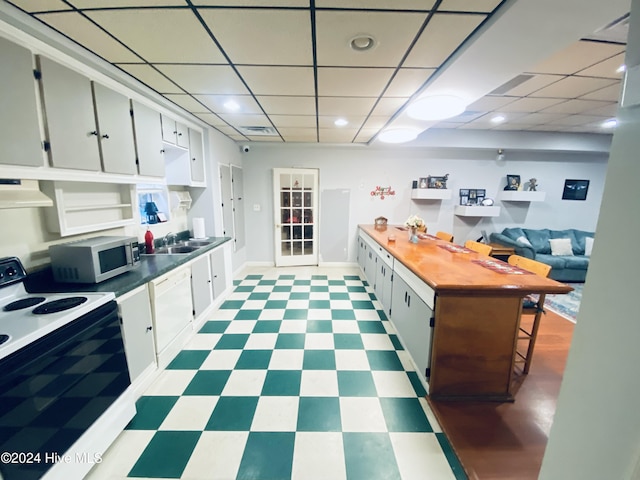 kitchen with a paneled ceiling, white appliances, white cabinets, sink, and extractor fan