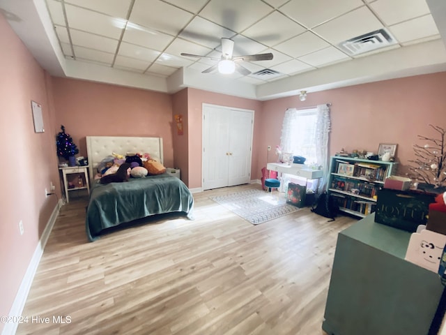 bedroom with a closet, ceiling fan, light hardwood / wood-style flooring, and a drop ceiling