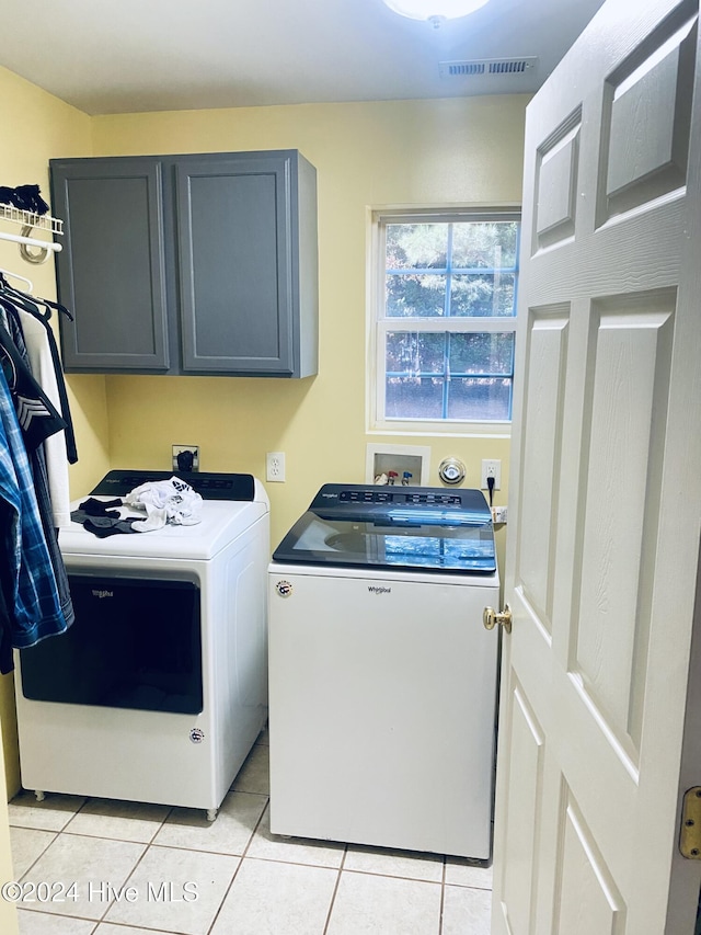 clothes washing area with cabinets, light tile patterned floors, and washing machine and clothes dryer