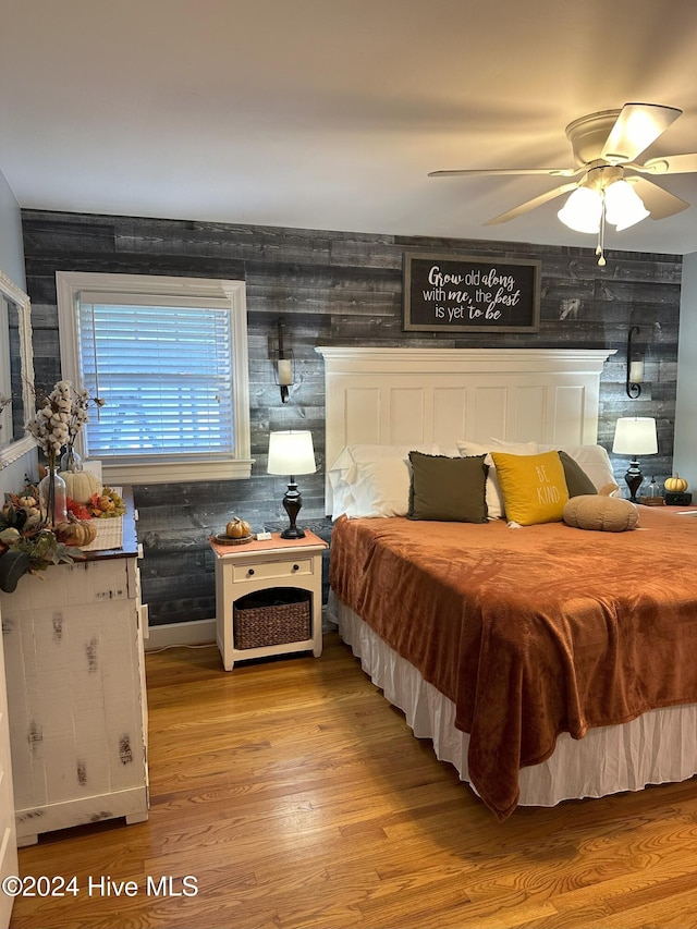 bedroom featuring ceiling fan, wood walls, and light wood-type flooring