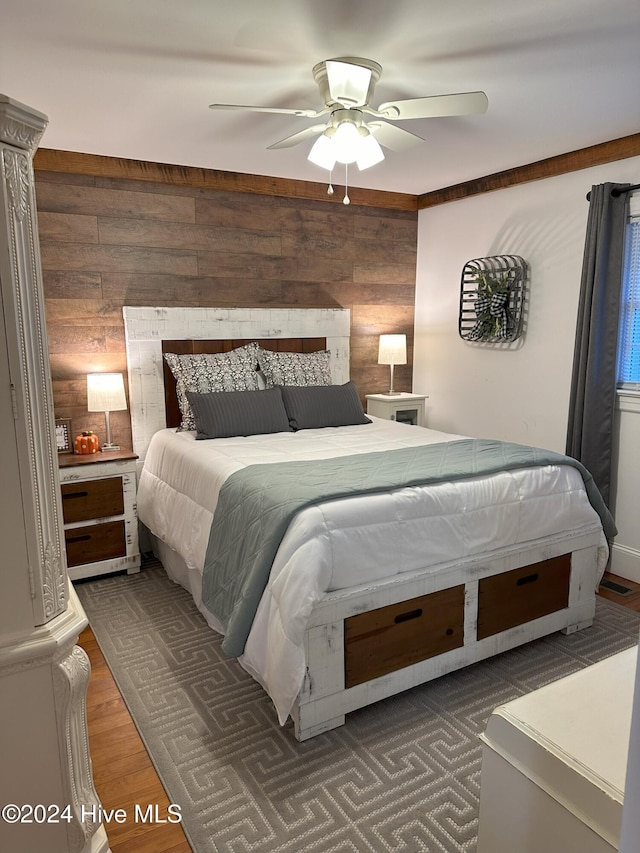bedroom with dark hardwood / wood-style floors, ceiling fan, and wooden walls