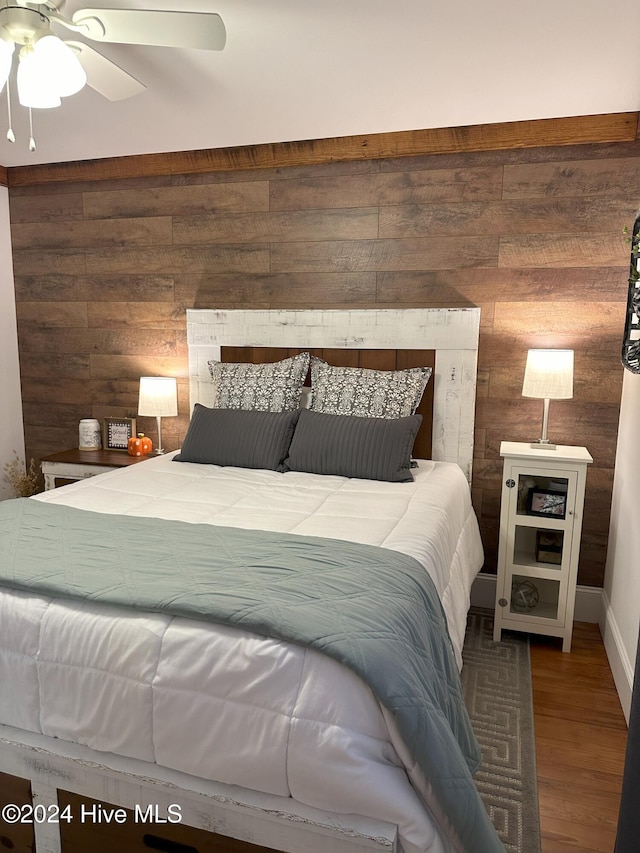 bedroom with wood walls, ceiling fan, and wood-type flooring