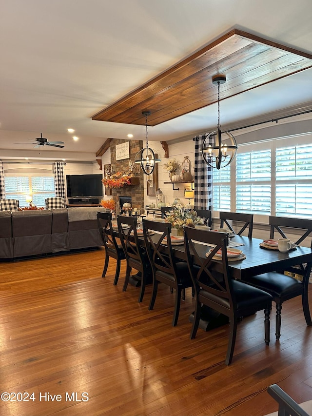 dining room featuring a fireplace, wood-type flooring, ceiling fan with notable chandelier, and plenty of natural light