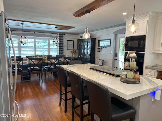kitchen with white cabinetry, black microwave, a breakfast bar area, and pendant lighting