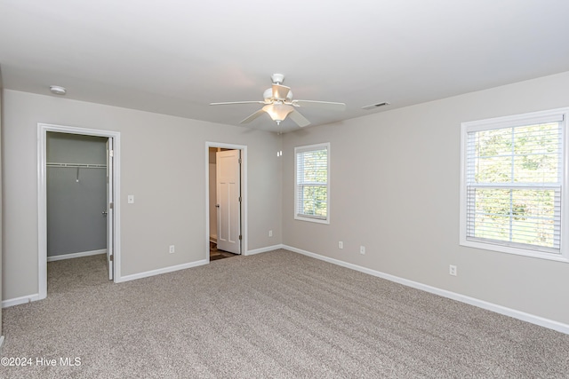 unfurnished bedroom featuring a closet, a walk in closet, carpet, and ceiling fan