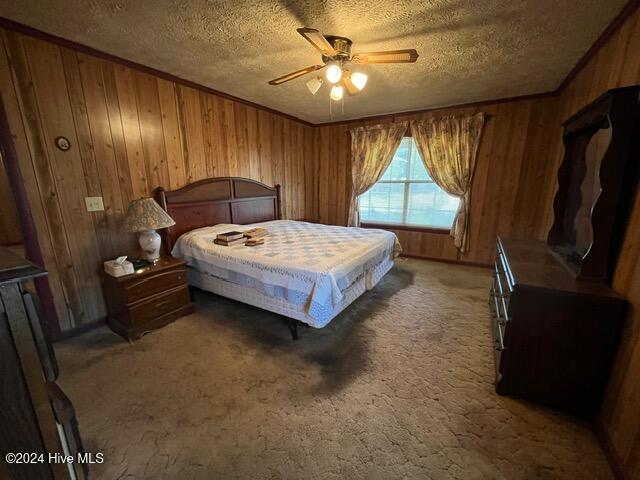 carpeted bedroom with wooden walls, a textured ceiling, ceiling fan, and crown molding