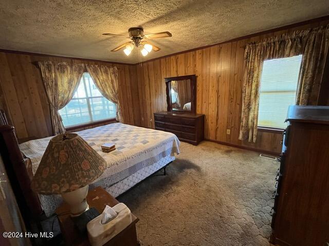 carpeted bedroom featuring a textured ceiling, ornamental molding, wooden walls, and ceiling fan