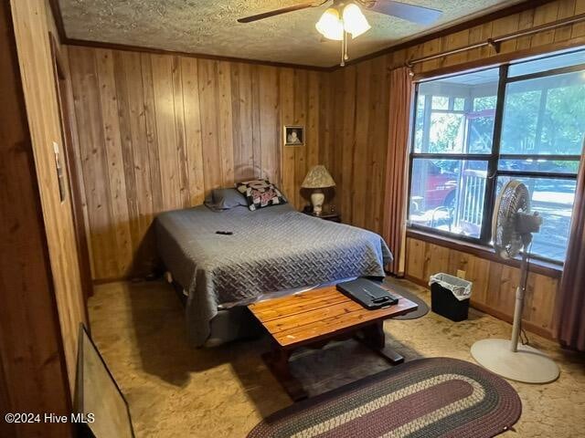 carpeted bedroom with a textured ceiling, wood walls, and ceiling fan