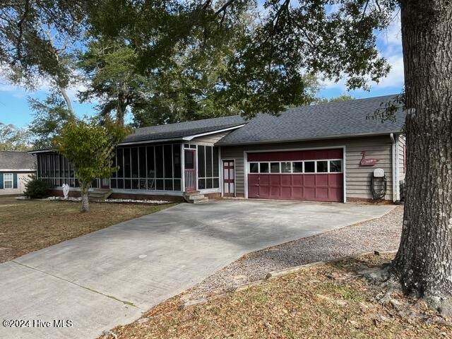 138 NW 17th St, Oak Island, NC 28465 - ranch-style house featuring a sunroom, a garage, concrete driveway, and roof with shingles