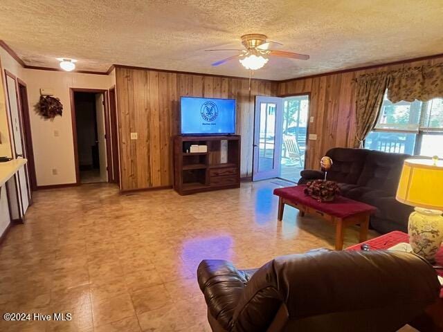 living room with ceiling fan, a healthy amount of sunlight, wooden walls, and ornamental molding