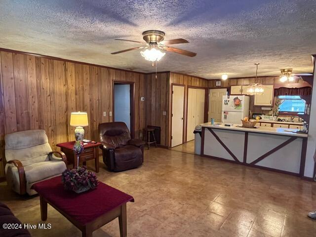 living room with wooden walls, a textured ceiling, and ceiling fan