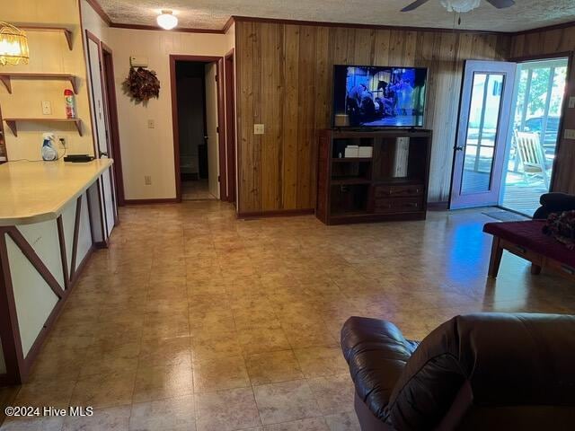 living room featuring wood walls, ceiling fan, a textured ceiling, and crown molding