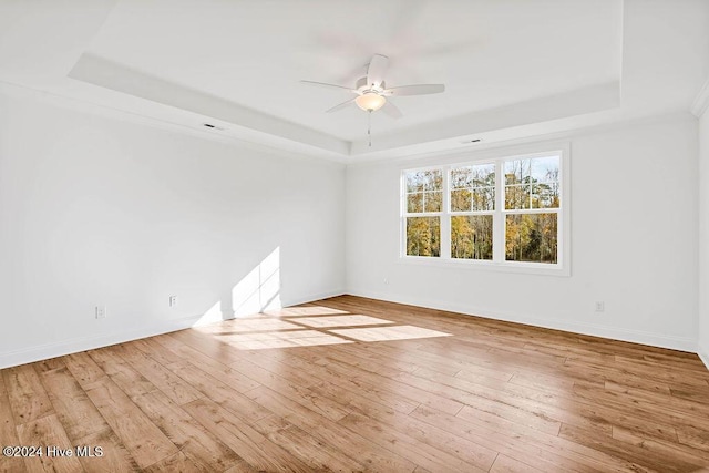 unfurnished room featuring ceiling fan, a raised ceiling, and light wood-type flooring