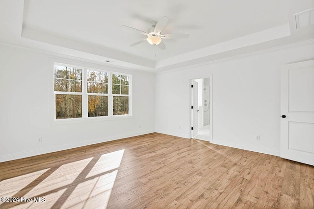 spare room with a raised ceiling, ceiling fan, and light hardwood / wood-style flooring