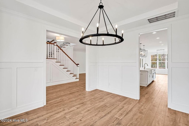 unfurnished dining area with crown molding, sink, an inviting chandelier, and light wood-type flooring