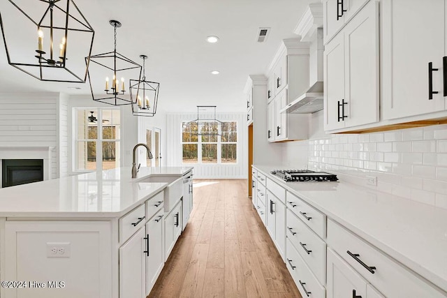 kitchen featuring pendant lighting, a kitchen island with sink, wall chimney exhaust hood, light wood-type flooring, and white cabinetry