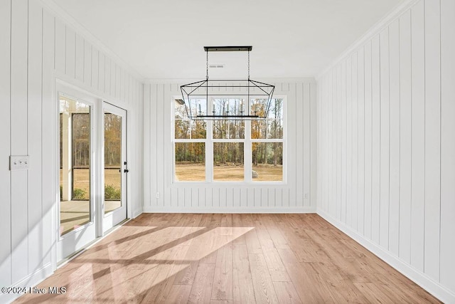 interior space with wood walls, light wood-type flooring, crown molding, and a chandelier