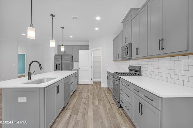 kitchen featuring stainless steel appliances, a kitchen island with sink, sink, pendant lighting, and light hardwood / wood-style floors