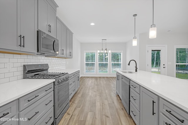 kitchen featuring appliances with stainless steel finishes, gray cabinetry, sink, light hardwood / wood-style flooring, and hanging light fixtures