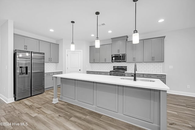 kitchen featuring a center island with sink, sink, gray cabinetry, and stainless steel appliances