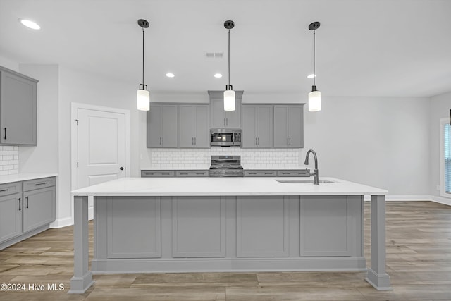 kitchen with gray cabinetry, stainless steel appliances, sink, a center island with sink, and light hardwood / wood-style floors