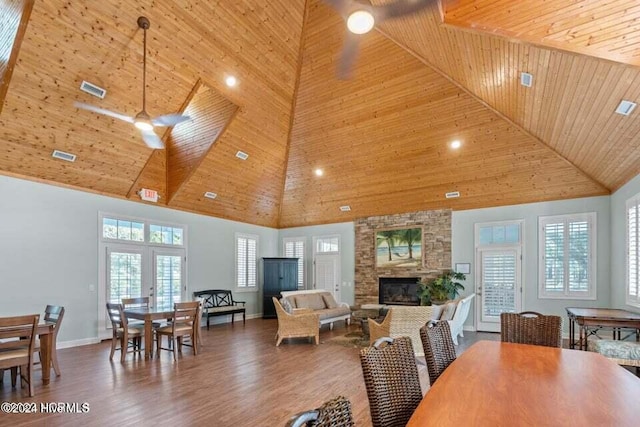 dining space featuring wooden ceiling, a high ceiling, a stone fireplace, ceiling fan, and dark hardwood / wood-style flooring