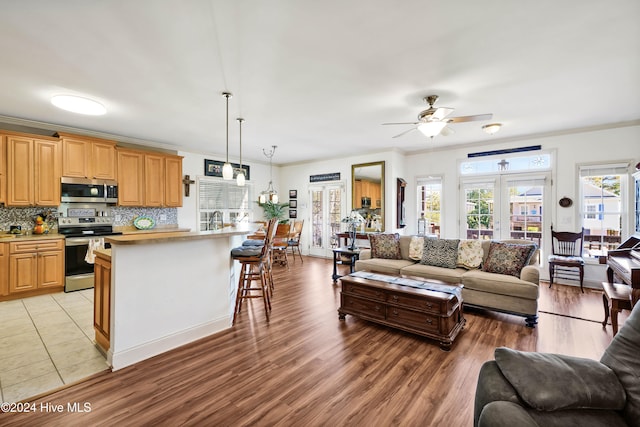 living room featuring ceiling fan, light wood-type flooring, ornamental molding, and a wealth of natural light