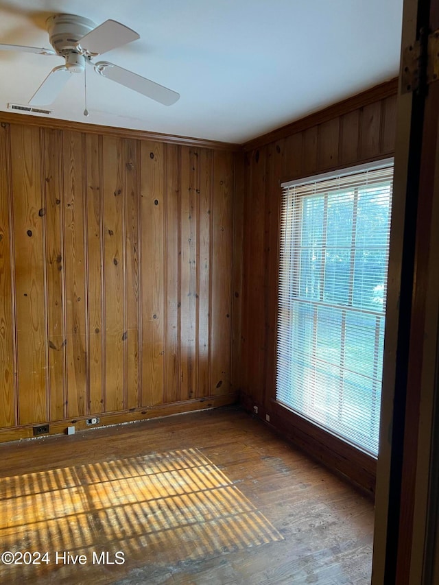 empty room with hardwood / wood-style floors, wooden walls, and ceiling fan