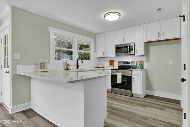 kitchen with appliances with stainless steel finishes, kitchen peninsula, sink, and white cabinets