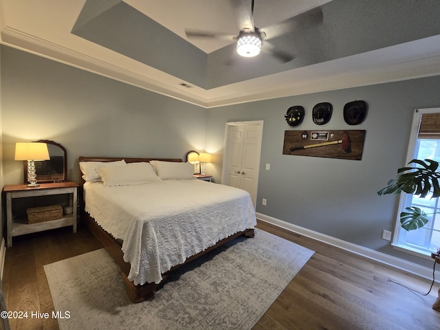 bedroom with crown molding, ceiling fan, baseboards, wood finished floors, and a raised ceiling