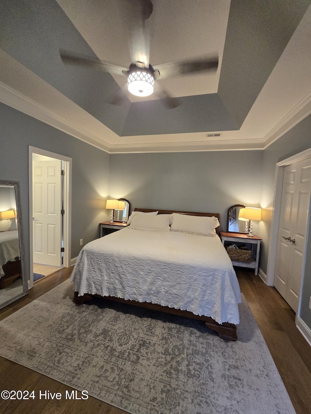 bedroom with a raised ceiling, wood finished floors, baseboards, and ornamental molding