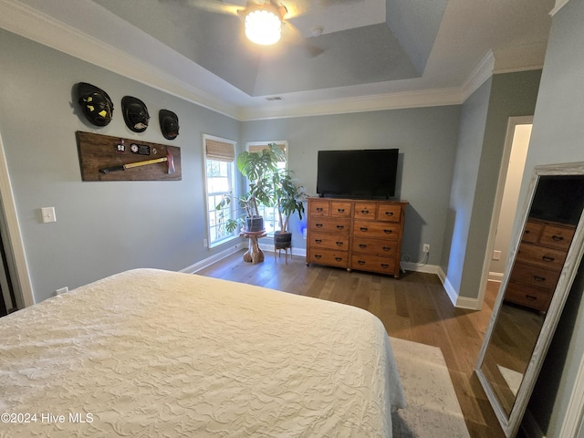 bedroom featuring visible vents, crown molding, baseboards, a tray ceiling, and wood finished floors