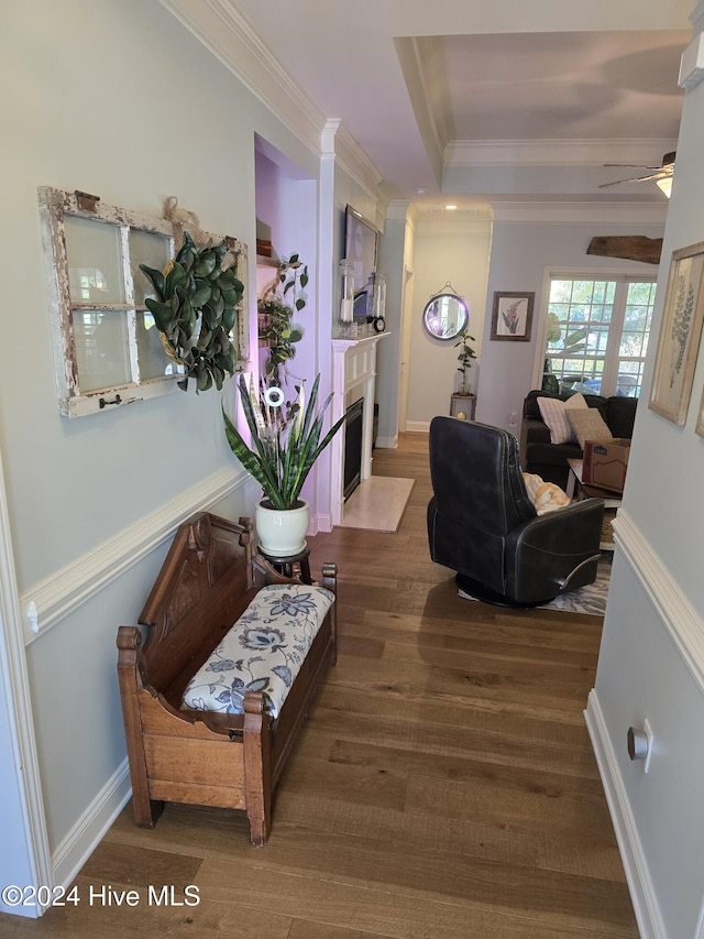 hallway featuring a raised ceiling, wood finished floors, baseboards, and ornamental molding