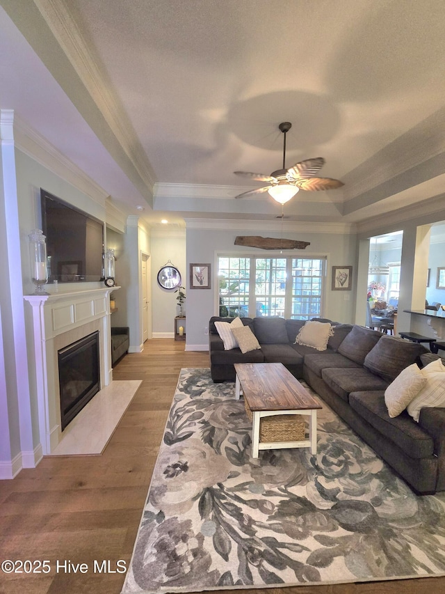 living area with a fireplace with flush hearth, wood finished floors, a raised ceiling, and ornamental molding