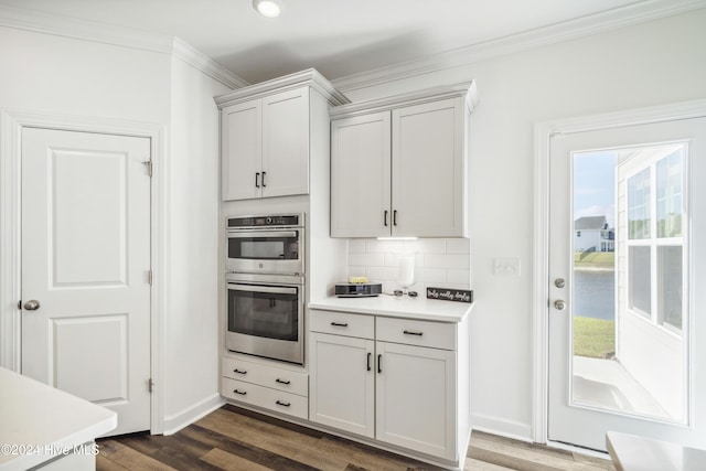 kitchen with crown molding, dark wood finished floors, double oven, light countertops, and decorative backsplash