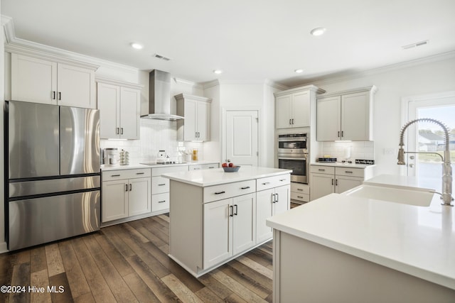 kitchen featuring visible vents, a kitchen island, wall chimney range hood, appliances with stainless steel finishes, and a sink