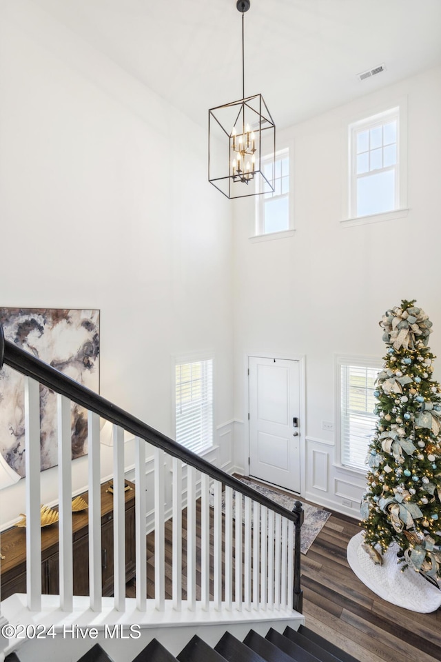 stairway with hardwood / wood-style floors, a towering ceiling, and an inviting chandelier