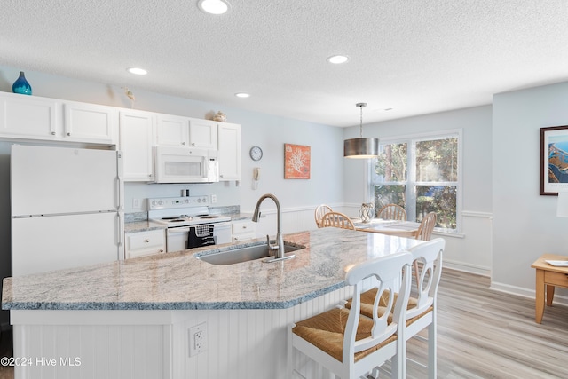 kitchen featuring sink, light hardwood / wood-style flooring, pendant lighting, white appliances, and white cabinets