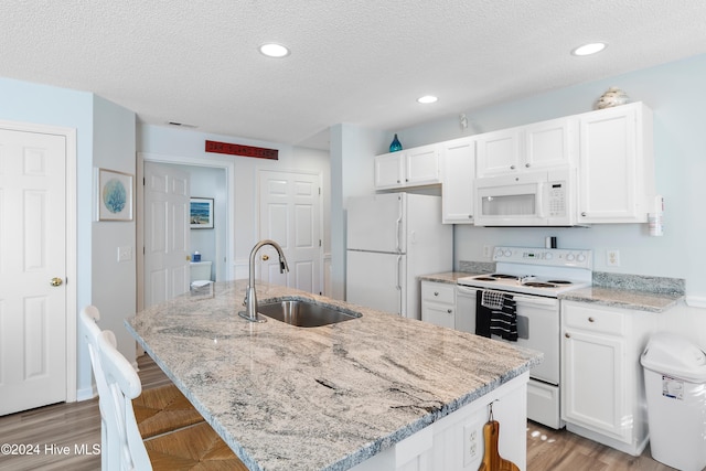 kitchen featuring sink, a kitchen island with sink, white appliances, a breakfast bar area, and light stone counters