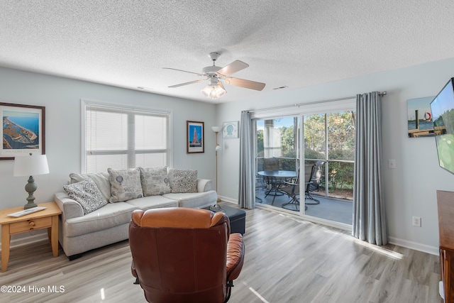 living room featuring ceiling fan, light wood-type flooring, and a textured ceiling