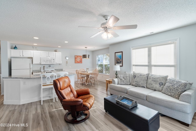 living room with light hardwood / wood-style flooring, ceiling fan, sink, and a textured ceiling