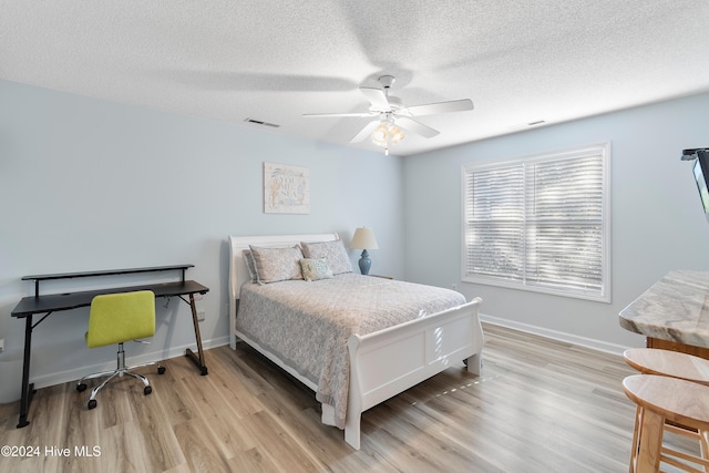 bedroom with ceiling fan, light wood-type flooring, and a textured ceiling