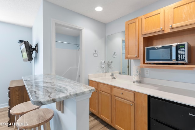 kitchen with light brown cabinetry, a breakfast bar, light hardwood / wood-style floors, and sink