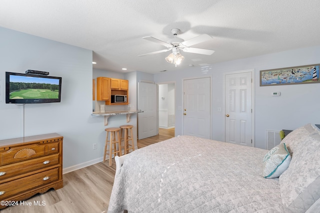 bedroom featuring multiple closets, ceiling fan, light hardwood / wood-style flooring, and a textured ceiling