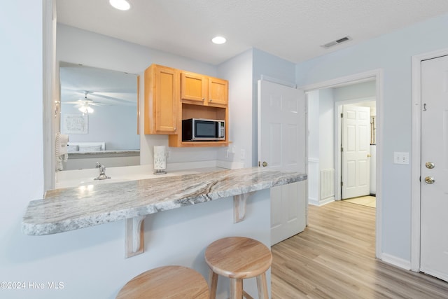 kitchen featuring a breakfast bar, kitchen peninsula, light brown cabinetry, and light wood-type flooring