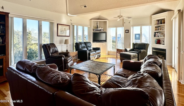 living room featuring lofted ceiling, ceiling fan, light wood-type flooring, and a textured ceiling