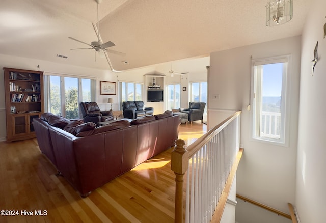 living room with hardwood / wood-style floors, a textured ceiling, vaulted ceiling, and ceiling fan