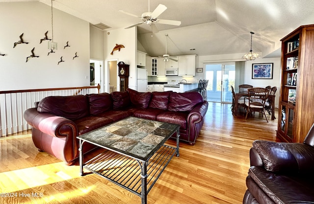 living room with ceiling fan with notable chandelier, a textured ceiling, light wood-type flooring, and high vaulted ceiling