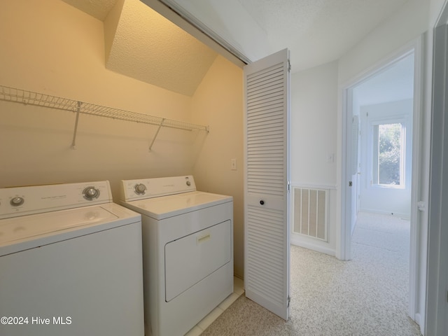 laundry area with washer and dryer, a textured ceiling, and light colored carpet