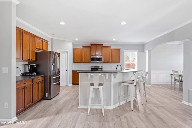 kitchen featuring appliances with stainless steel finishes, a kitchen breakfast bar, a kitchen island with sink, crown molding, and light hardwood / wood-style flooring